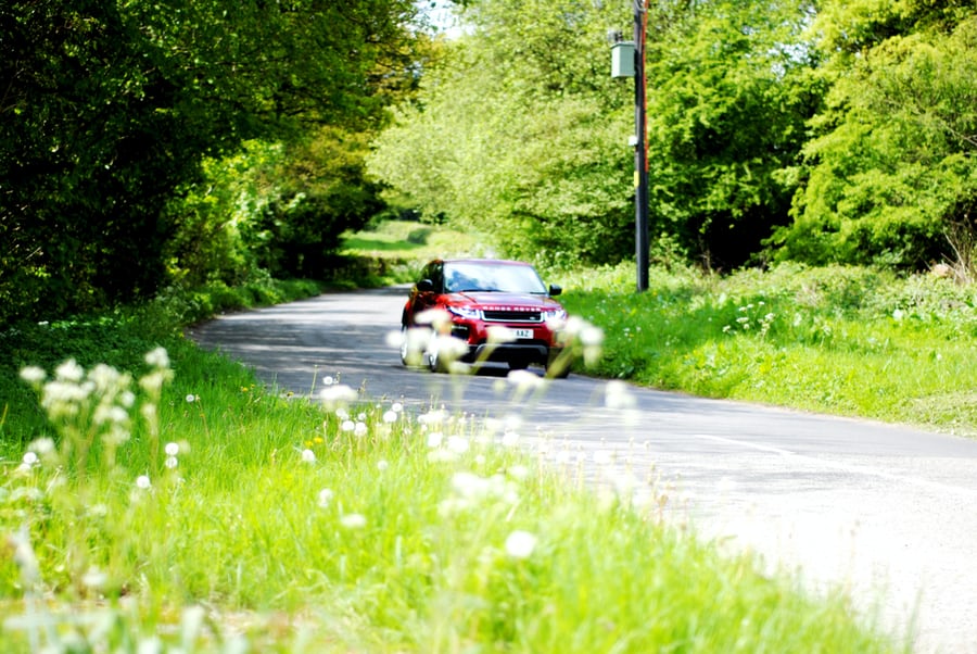 Car driving along a narrow green country lane bordered by hedgerows in summer